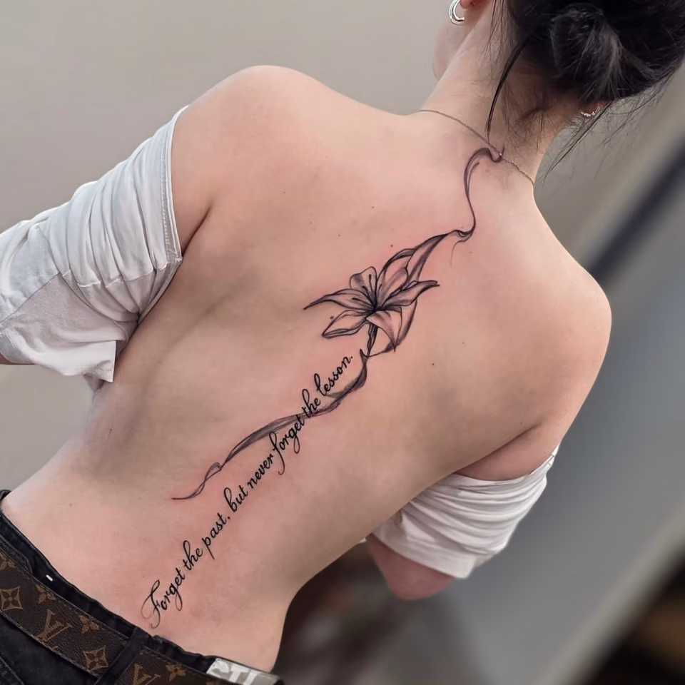Lilie mit Schriftzug Forget the past, but never forget the lesson entlang der Wirbelsäule